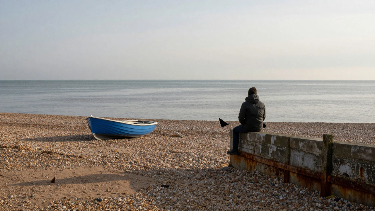 Empty pebble beach at Tankerton Sands at dusk, solitary figure on stone wall, quiet sea stretching to horizon.